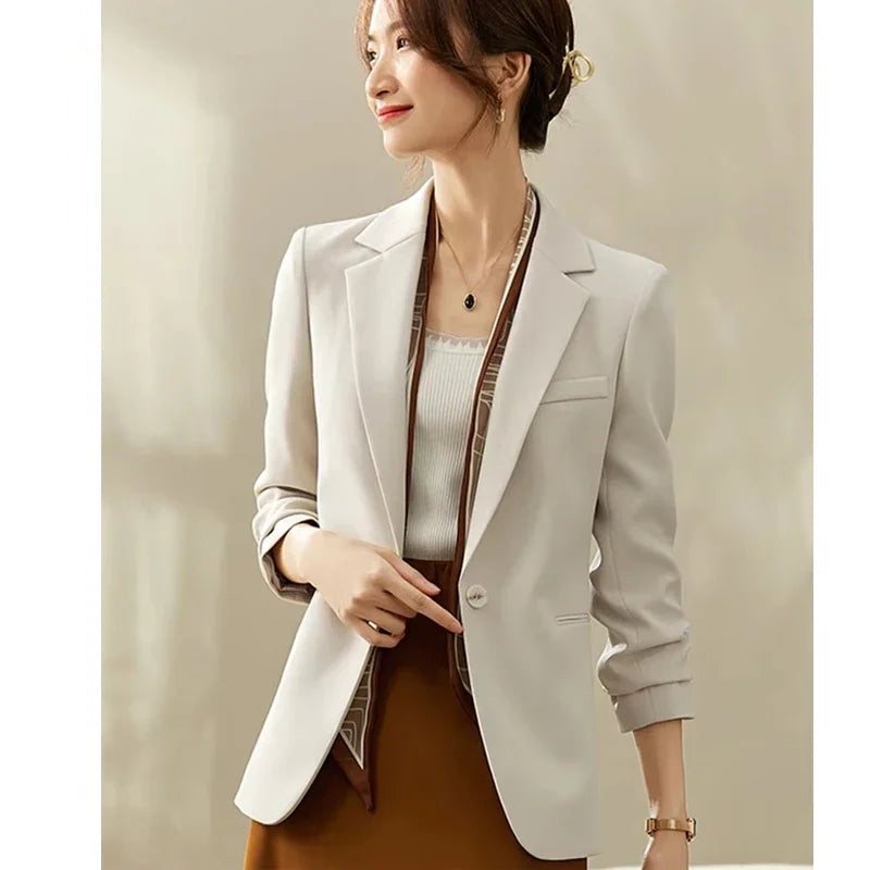 Woman wearing a light gray blazer over a patterned dress on a beige background